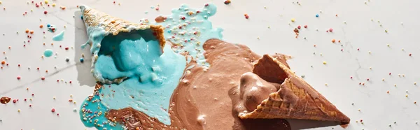 Delicioso chocolate derretido y helado azul en conos de gofre sobre fondo gris mármol con aspersiones, plano panorámico - foto de stock