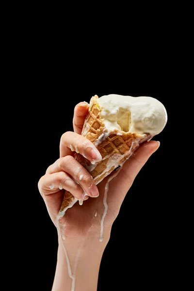 Vue partielle de femme tenant fondant délicieuse crème glacée à la vanille dans un cône de gaufre croustillant isolé sur noir — Photo de stock