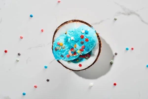 Top view of delicious blue ice cream with sprinkles on coconut half on marble grey background — Stock Photo