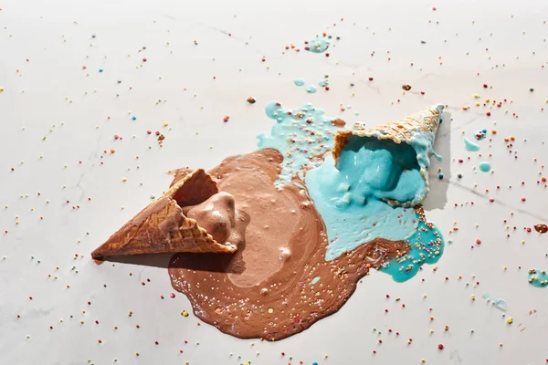 Vue de dessus de délicieux chocolat fondu et crème glacée bleue dans des cônes de gaufres sur fond gris marbre avec des aspersions — Photo de stock