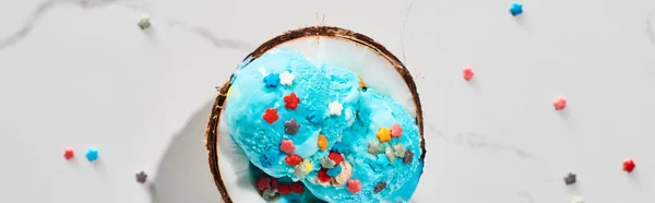 Top view of delicious blue ice cream with sprinkles on coconut half on marble grey background, panoramic shot — Stock Photo