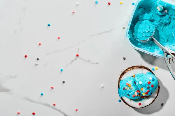 Top view of delicious blue ice cream with sprinkles on coconut half and ice cream spoon on marble grey background — Stock Photo