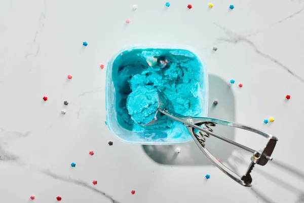 Vue du dessus de délicieuse crème glacée bleue avec saupoudrer en boîte avec cuillère à crème glacée sur fond gris marbre — Photo de stock