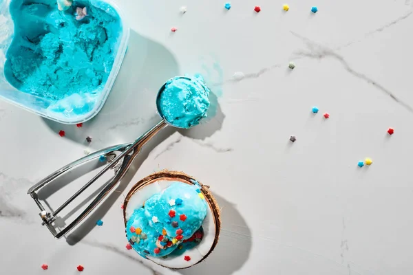 Top view of delicious blue ice cream with sprinkles on coconut half and in ice cream spoon on marble grey background — Stock Photo