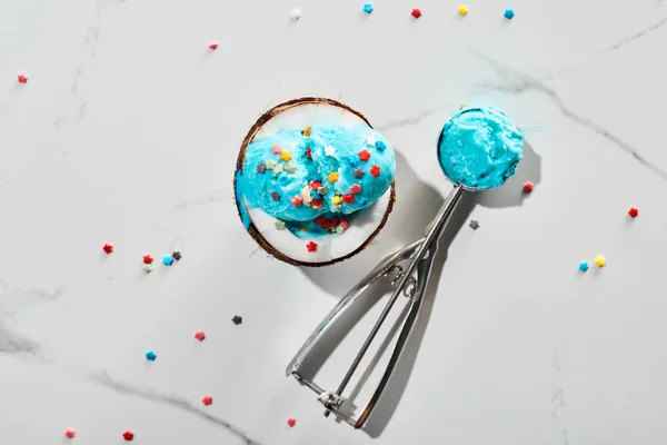 Вид сверху на свежее голубое мороженое с брызгами на кокосовой половинке и в ложке мороженого на мраморном сером фоне — стоковое фото