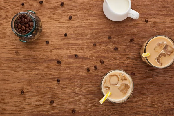 Draufsicht auf Eiskaffee in Gläsern, Milch- und Kaffeekörner auf Holztisch — Stockfoto