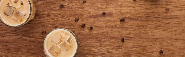 Top view of ice coffee and coffee grains scattered on wooden table, panoramic shot — Stock Photo