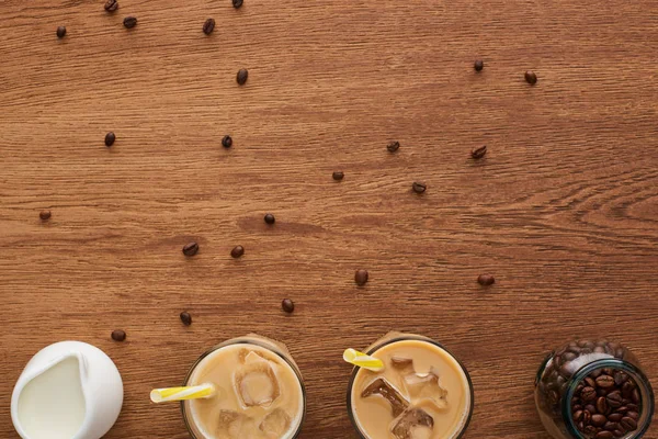 Vue du dessus du café dans des verres avec glace et paille, lait et grains de café sur table en bois avec espace de copie — Photo de stock