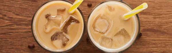 Top view of fresh ice coffee in glasses with straws and coffee grains on wooden table, panoramic shot — Stock Photo