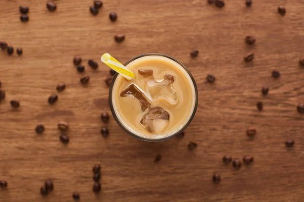 Selective focus of ice coffee with straw in glass and coffee grains on wooden table — Stock Photo