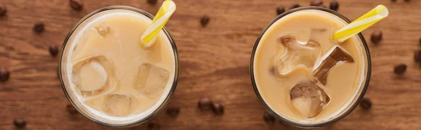 Selective focus of ice coffee with straws in glasses and coffee grains on wooden table, panoramic shot — Stock Photo