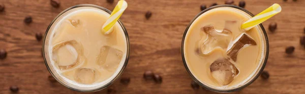 Enfoque selectivo de café helado con pajitas en vasos y granos de café en mesa de madera, plano panorámico - foto de stock