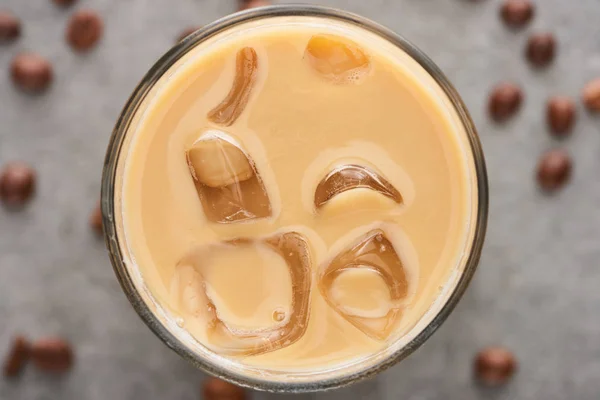 Закрытый вид на ледяной кофе в стакане с соломой и зерном кофе на сером фоне — стоковое фото