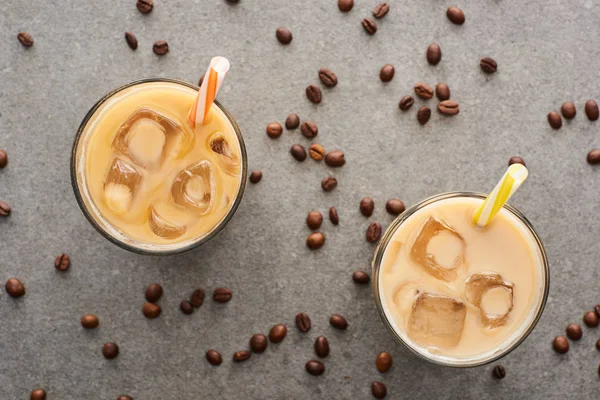 Vue de dessus du café glacé avec des pailles et des grains de café sur fond gris — Photo de stock