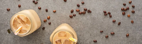 Vista dall'alto di ghiaccio fresco caffè in vasetti di vetro con cannucce e chicchi di caffè su fondo grigio, colpo panoramico — Foto stock