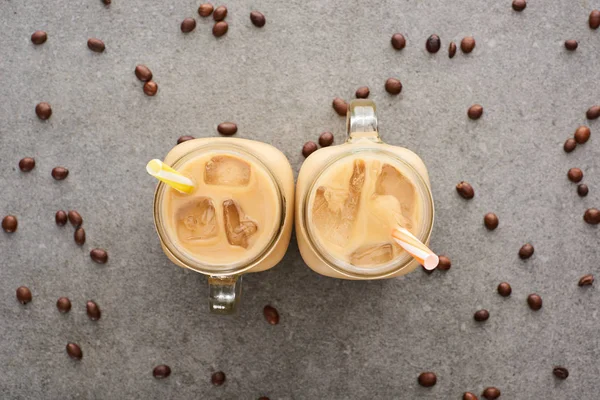 Vue du dessus du café glacé dans des bocaux en verre avec des pailles et des grains de café sur fond gris — Photo de stock