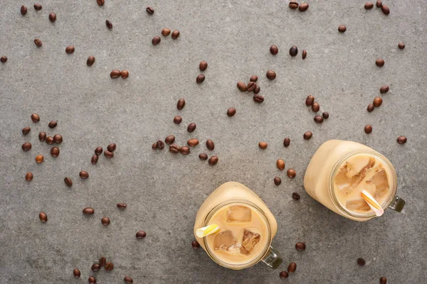 Vue du dessus du café glacé dans des bocaux en verre avec des pailles et des grains de café éparpillés sur fond gris — Photo de stock