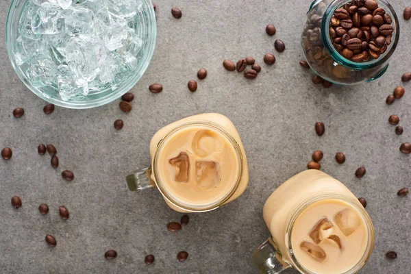 Ansicht von Eiskaffee in Glasgefäßen in der Nähe von Kaffeekörnern und Eiswürfeln auf grauem Hintergrund — Stockfoto