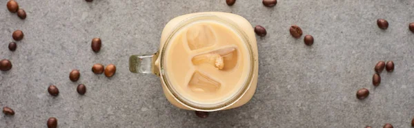 Top view of ice coffee in glass jar near coffee grains on grey background, panoramic shot — Stock Photo
