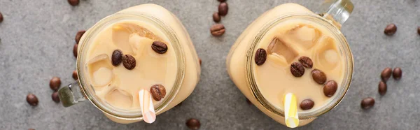 Top view of ice coffee in glass jars with straws and coffee grains on grey background, panoramic shot — Stock Photo