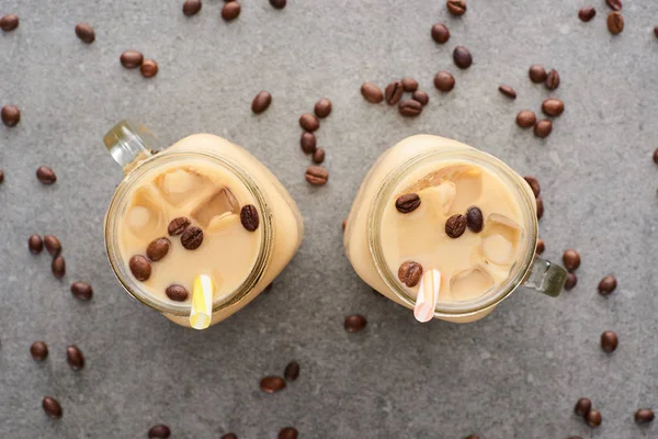 Vue du dessus du café glacé dans des bocaux en verre avec des pailles et des grains de café sur fond gris — Photo de stock