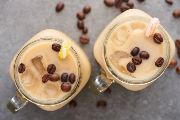 Selective focus of ice coffee in glass jar with straw near coffee grains on grey background — Stock Photo