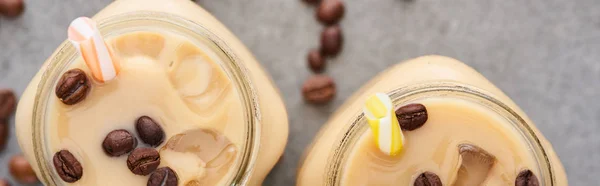 Selective focus of ice coffee in glass jar with straw near coffee grains on grey background, panoramic shot — Stock Photo