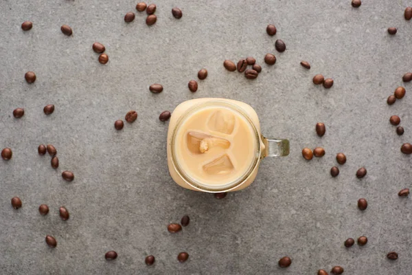 Top view of delicious ice coffee in glass jar near coffee grains on grey background — Stock Photo