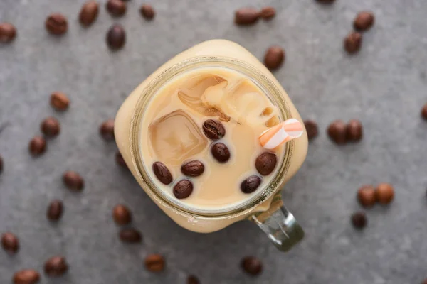 Selective focus of ice coffee in glass jar with straw near coffee grains on grey background — Stock Photo