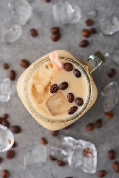 Selective focus of ice coffee in glass jar with straw near coffee grains and ice cubes on grey background — Stock Photo