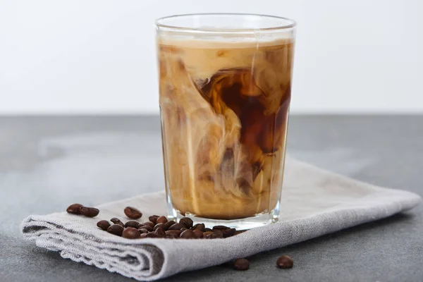 Café gelado misturando com leite em vidro em guardanapo com grãos de café isolados em branco — Fotografia de Stock