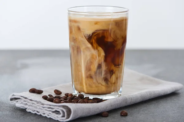 Café helado mezclado con leche en vaso en servilleta con granos de café aislados en blanco - foto de stock