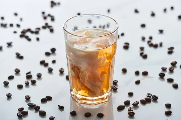 Foyer sélectif de mélange de café glacé avec du lait dans le verre près de grains de café dispersés sur fond gris — Photo de stock