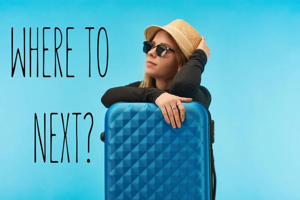 Blonde girl in sunglasses and straw hat near blue suitcase isolated on blue with where to next question — Stock Photo