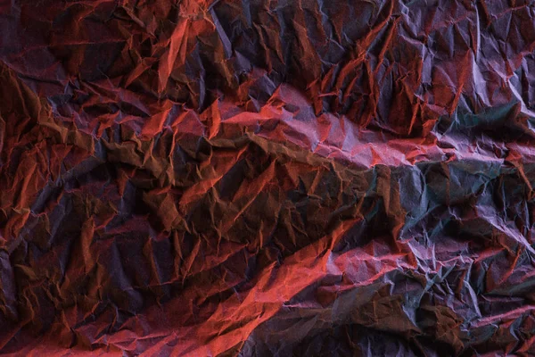 Vista superior de papel amassado com iluminação colorida rosa e vermelha na escuridão — Fotografia de Stock