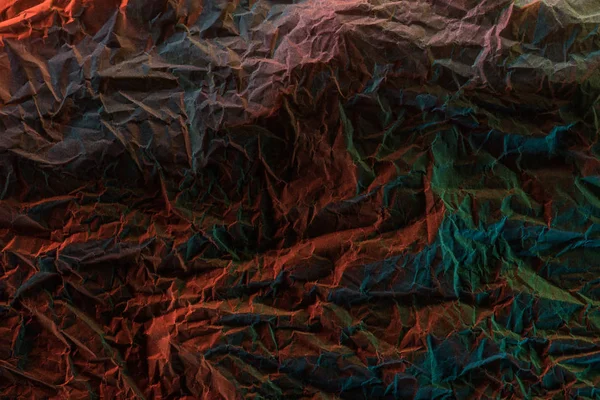 Top view of crumpled textured paper with multicolored lighting in darkness — Stock Photo