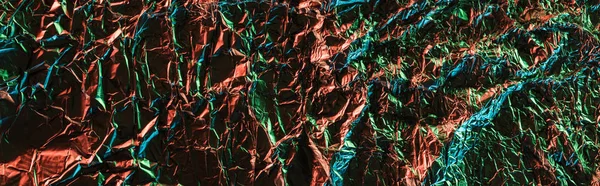 Panoramic shot of glossy crumpled foil with colorful lighting reflection in darkness — Stock Photo