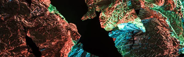 Panoramic shot of torn foil with colorful lighting in darkness isolated on black — Stock Photo