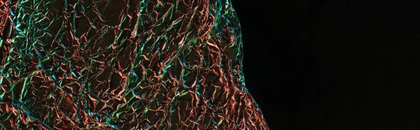 Panoramic shot of crumpled foil with colorful lighting isolated on black — Stock Photo