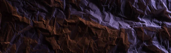 Panoramic shot of crumpled paper with purple colorful lighting in darkness — Stock Photo