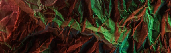 Tiro panorâmico de papel amassado com iluminação colorida verde na escuridão — Fotografia de Stock