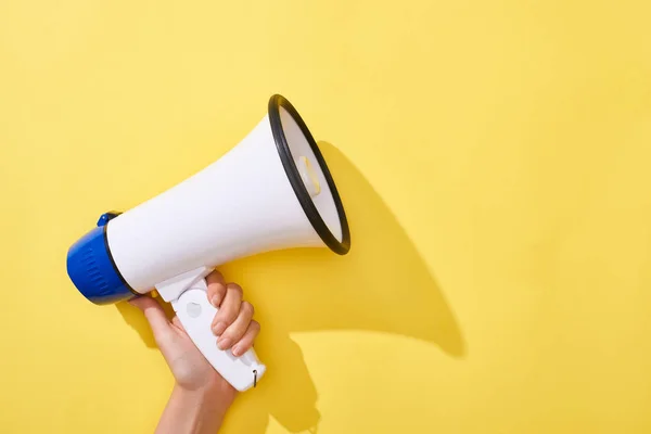 Cropped view of woman holding loudspeaker on yellow background — Stock Photo