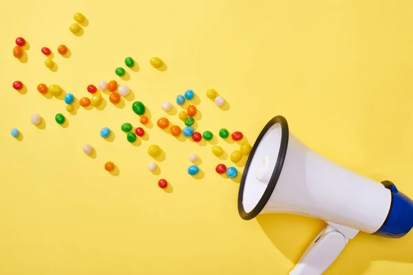 Top view of loudspeaker with colorful candies on yellow background — Stock Photo