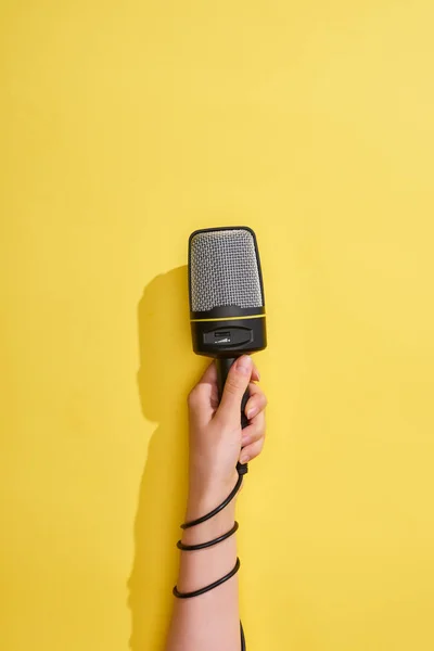 Vista ritagliata della donna che tiene il microfono su sfondo giallo — Foto stock