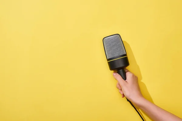 Cropped view of woman holding microphone on yellow background — Stock Photo