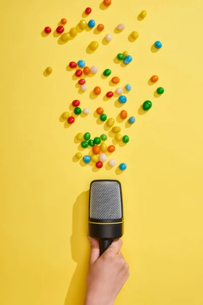 Cropped view of woman holding microphone with colorful candies on yellow background — Stock Photo