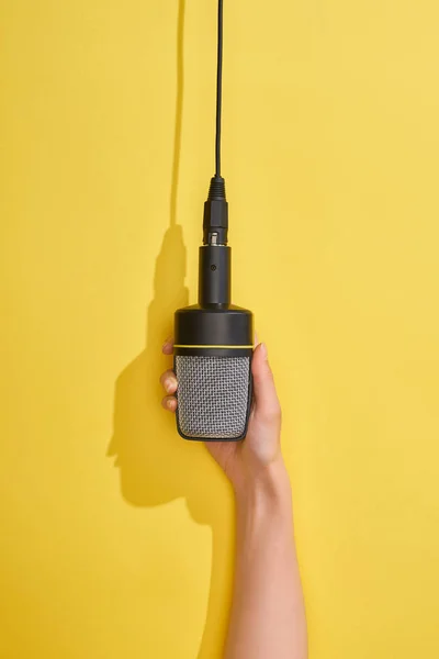 Cropped view of woman holding microphone on yellow background — Stock Photo