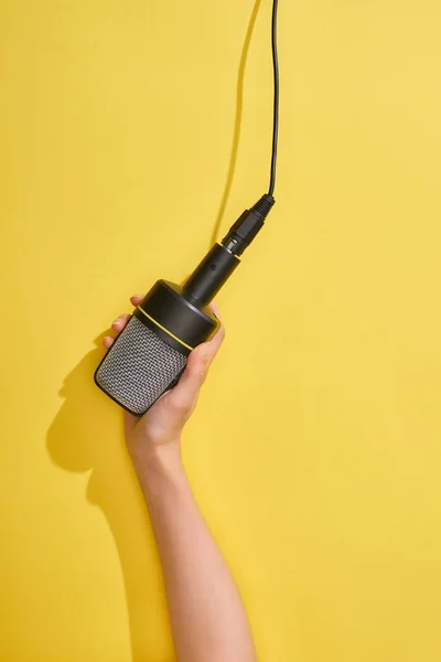 Vista ritagliata della donna che tiene il microfono su sfondo giallo — Foto stock