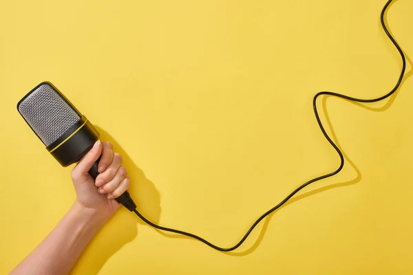 Vista ritagliata della donna che tiene il microfono su sfondo giallo — Foto stock