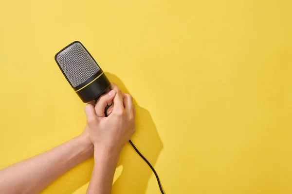 Cropped view of woman holding microphone on yellow background — Stock Photo
